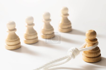 Téléchargez les photos : Gros plan d'une corde blanche enchevêtrée autour d'un pion d'échecs en bois avec plusieurs échiquiers à proximité. Concept de faire face aux difficultés de la vie et d'être accablé par la responsabilité. - en image libre de droit