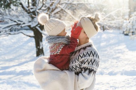 Foto de Joven madre y su lindo hijo pequeño usando suéteres calientes jugando peekaboo durante el día de invierno soleado - Imagen libre de derechos