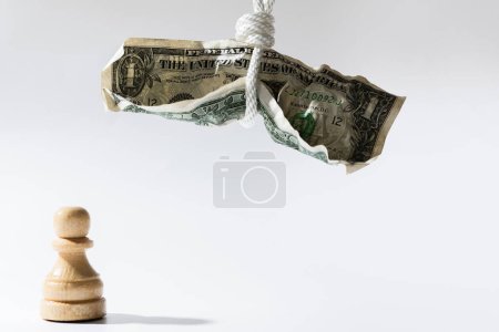 Foto de Un billete de un dólar arrugado colgado en una cuerda blanca con un ajedrecista de madera parado debajo. Concepto de fraude monetario, pagos fiscales o de crédito. - Imagen libre de derechos