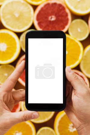 Téléchargez les photos : Gros plan de main femme tenant smartphone avec écran vide pour votre conception sur fond d'agrumes - en image libre de droit