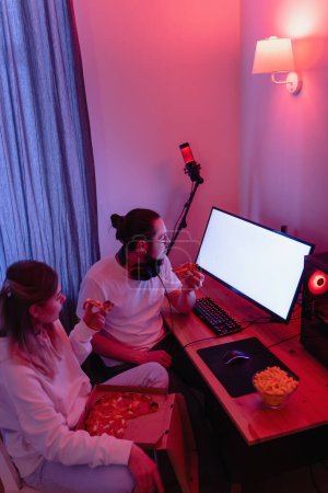Foto de Pareja joven relajándose en casa en la habitación con luz de neón y comiendo pizza, viendo películas en línea o jugando videojuegos - Imagen libre de derechos