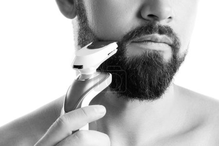 Foto de Hombre barbudo guapo está utilizando trimmer eléctrico sobre fondo blanco - Imagen libre de derechos