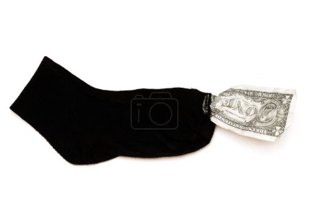 Foto de Primer plano de un viejo calcetín negro con un billete de un dólar que sobresale del agujero sobre fondo blanco. Concepto de pobreza y crisis financiera. - Imagen libre de derechos