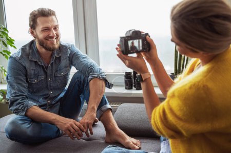 Téléchargez les photos : Jeune femme photographe prenant des photos de son petit ami à la maison - en image libre de droit