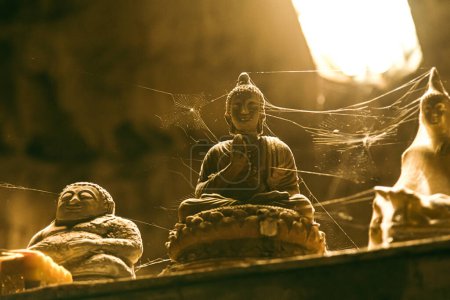 Téléchargez les photos : Gros plan d'une statue de pierre de Bouddha longtemps oubliée, recouverte de toile d'araignée, dans une grotte. - en image libre de droit