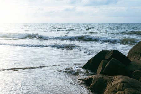 Téléchargez les photos : Vagues de mer mousseuses s'écrasant sur une plage de sable pendant la marée haute avec ciel nuageux en arrière-plan. - en image libre de droit