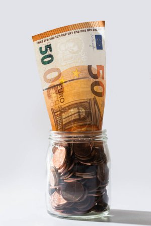 Foto de Primer plano de un billete de 50 euros dentro de un frasco de vidrio lleno de monedas de cobre. - Imagen libre de derechos