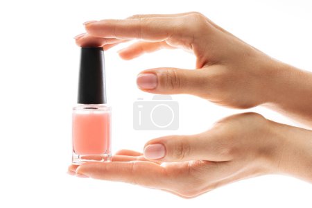 Foto de Primer plano de las manos femeninas con hermosa manicura francesa sosteniendo botella de esmalte de uñas rosa sobre fondo blanco - Imagen libre de derechos