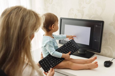 Téléchargez les photos : Petit garçon curieux intéressé par l'activité de sa mère pigiste est assis sur un bureau et la distraire du travail sur ordinateur. - en image libre de droit