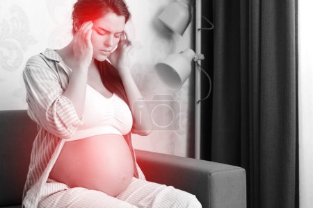 Photo for Young pregnant woman sitting on the sofa at home with a painful headache - Royalty Free Image