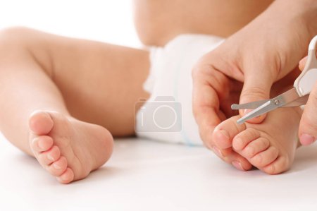 Téléchargez les photos : Gros plan d'une mère tenant doucement le pied de son petit enfant et coupant des ongles sur fond blanc. - en image libre de droit