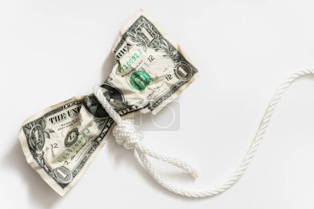 Téléchargez les photos : Corde blanche enchevêtrée autour d'un billet d'un dollar froissé. Notion de fraude monétaire, de paiement de dettes ou de crédits. - en image libre de droit