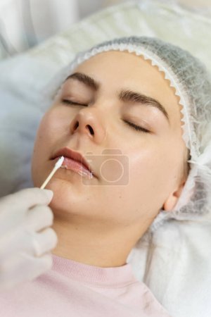 Photo for Professional permanent makeup artist applying anesthetic on client's lips before lip blushing procedure - Royalty Free Image