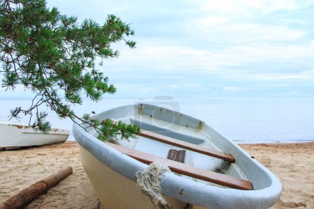 Photo for Closeup shot of a abandoned shabby fishing boats lying on a sandy beach near the calm sea water. - Royalty Free Image