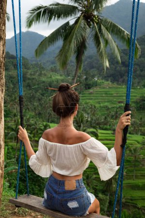 Foto de Mujer joven en columpios de cuerda con hermosa vista en terrazas de arroz en el Bali. - Imagen libre de derechos
