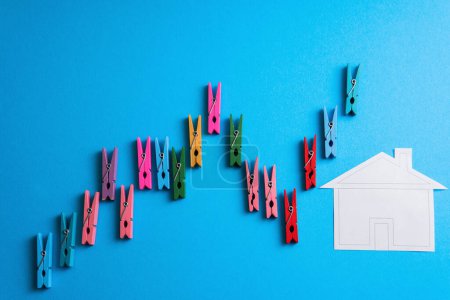 Photo for Closeup shot of a financial graph made of colorful wooden clothespins and a wooden house applique on blue background. - Royalty Free Image