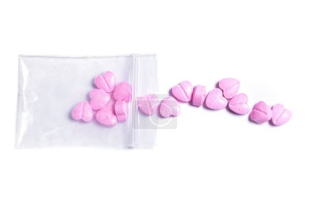 Foto de Primer plano de una bolsa de cierre transparente y píldoras en forma de corazón rosa sobre fondo blanco. - Imagen libre de derechos