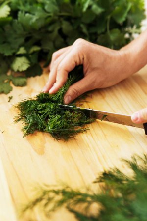 Photo for Closeup of female hands with knife chopping dill on wooden cutting board - Royalty Free Image