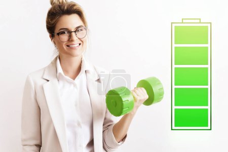 Photo for Energized business woman lifting green dumbbell. Fully charged battery symbol beside. Concepts of active life, stress free work and uplifting. - Royalty Free Image