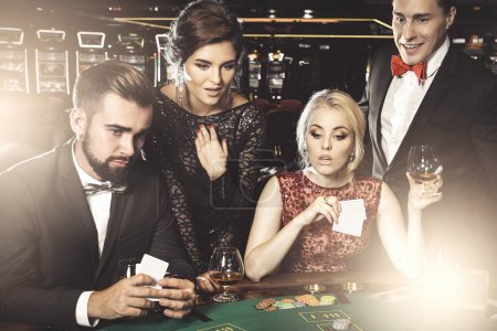 Téléchargez les photos : Groupe de jeunes riches jouant au poker et buvant du cognac dans le casino - en image libre de droit