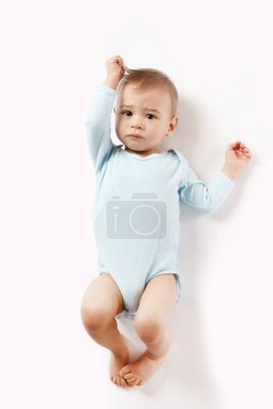 Foto de Adorable niño en un mameluco está acostado sobre su espalda y mirando sobre fondo blanco. - Imagen libre de derechos