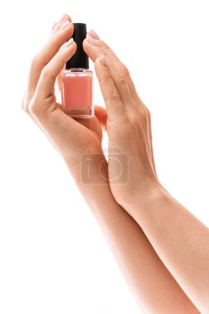 Foto de Primer plano de las manos femeninas con hermosa manicura francesa sosteniendo botella de esmalte de uñas rosa sobre fondo blanco - Imagen libre de derechos