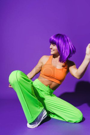Foto de Bailarina activa despreocupada que usa ropa deportiva colorida que actúa contra el fondo púrpura - Imagen libre de derechos