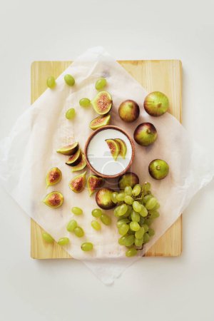 Foto de Delicioso yogur griego natural en tazón de barro con higos y uva sobre papel pergamino blanco - Imagen libre de derechos