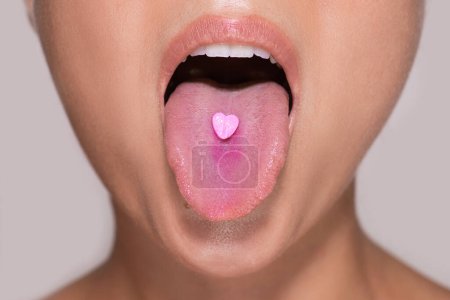 Photo for Closeup shot of a bottom part of a young female face with a pink heart shaped pill on her tongue. - Royalty Free Image