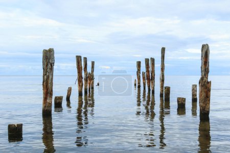 Foto de Una hermosa toma de un paisaje marino tranquilo con los postes rotos del muelle que sobresalen del agua en el fondo del horizonte. - Imagen libre de derechos
