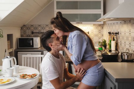Photo for Young and sensual couple waiting for a baby. Husband and his pregnant wife during breakfast time in cozy kitchen. - Royalty Free Image