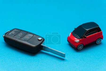 Téléchargez les photos : Clé de voiture étendue noire et voiture jouet rouge sur fond bleu - en image libre de droit