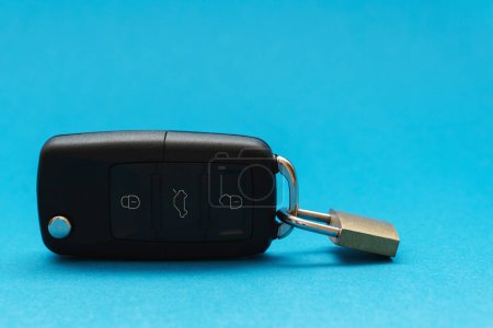 Téléchargez les photos : Cadenas attaché à une clé de voiture noire sur fond bleu. Concept d'assurance. - en image libre de droit
