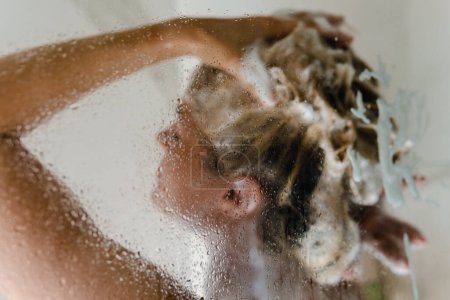 Téléchargez les photos : Jeune femme se lave les cheveux avec un shampooing tout en prenant une douche - en image libre de droit