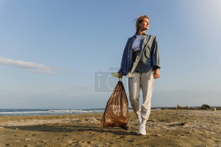 Foto de Mujer feliz voluntaria está recogiendo residuos de plástico en la playa para contribuir al esfuerzo de mantener la naturaleza limpia. - Imagen libre de derechos