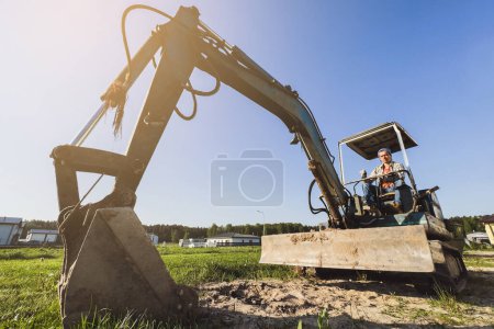 Téléchargez les photos : Jeune homme conduisant sa vieille pelle pendant son travail sur un chantier. - en image libre de droit