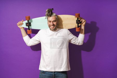 Foto de Retrato de hombre alegre de mediana edad con longboard con sudadera blanca sobre fondo púrpura - Imagen libre de derechos