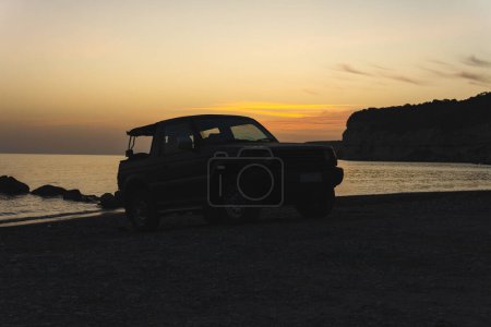 Téléchargez les photos : Silhouette coucher de soleil d'un 4x4 convertible sur une plage de galets. Plage de Kourion - Chypre - en image libre de droit