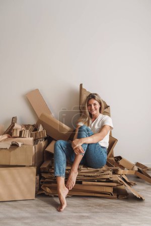 Téléchargez les photos : Jeune femme baguette tas de déchets de carton à la maison. Concepts du recyclage du papier et du tri des déchets. - en image libre de droit