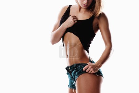 Foto de Joven mujer fitness con pantalones cortos de jean está mostrando sus abdominales musculosos sobre fondo blanco. - Imagen libre de derechos
