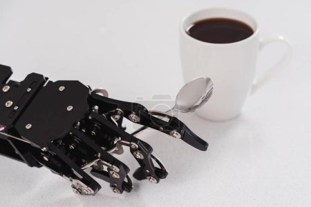 Téléchargez les photos : Véritable main robot avec cuillère et tasse de café blanche. Concept d'automatisation robotique des processus. - en image libre de droit