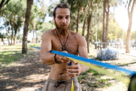 Photo for Young man setting up slacklining equipment in city park during summer day - Royalty Free Image
