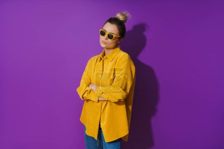 Photo for Portrait of young  girl wearing yellow shirt and sunglasses showing disdain expression against purple background - Royalty Free Image