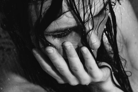 Téléchargez les photos : Portrait monochrome de femme triste et humide avec un maquillage maculé sur le visage sous la douche - en image libre de droit