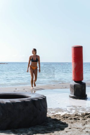 Photo for Confident woman athlete walk out the sea near a beach gym. - Royalty Free Image