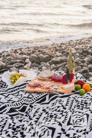 Photo for Sunset picnic with gourmet delights and wine on a pebble beach. - Royalty Free Image