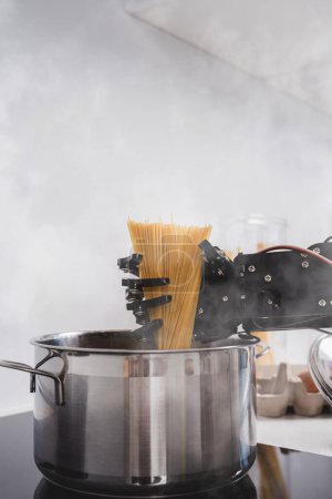 Foto de La mano real del robot agrega espaguetis en la olla con agua hirviendo. Concepto de automatización robótica de procesos. - Imagen libre de derechos