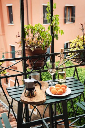 Téléchargez les photos : Nature morte de la casserole Moka, tasse de café, abricots et bouteille de vin blanc sur une petite table au balcon - en image libre de droit