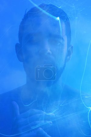 Téléchargez les photos : Portrait créatif de jeune homme beau avec brume et lumière bleue. - en image libre de droit