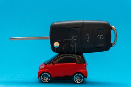 Téléchargez les photos : Clé de voiture noire sur le dessus de la voiture jouet rouge sur le fond bleu - en image libre de droit